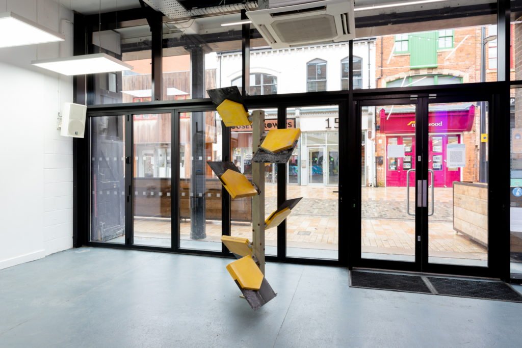 WayPoint, a sculpture by Leo Fitzmaurice in Gallery Café. The structure is made of six yellow and black Pay Point Company signs with logos removed.